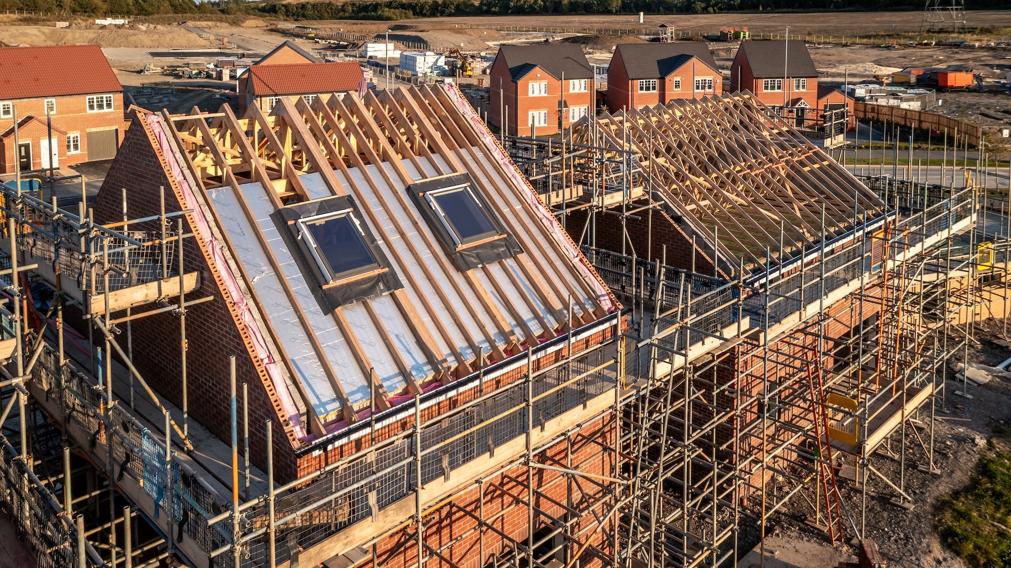 New Build House Construction Aerial view of a roof under construction with beams and apex supporting exterior skylight windows on a new build house surrounded by scaffolding on a construction site